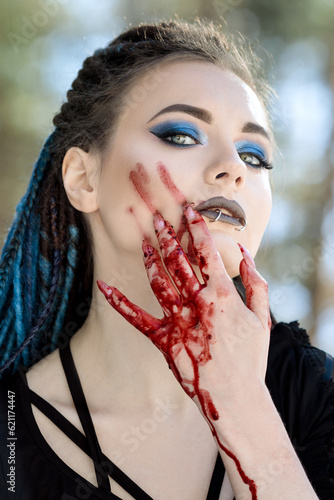 girl in black with blue hair dreadlocks paints her face blood