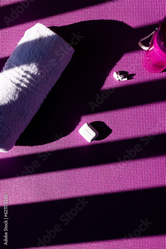 Vertical image of bottle of water, towel, earphones lying on mat on sunny day