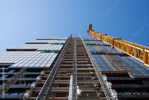 Looking up at the construction site of a skyscraper building with a yellow crane an an exterior elevator  photo