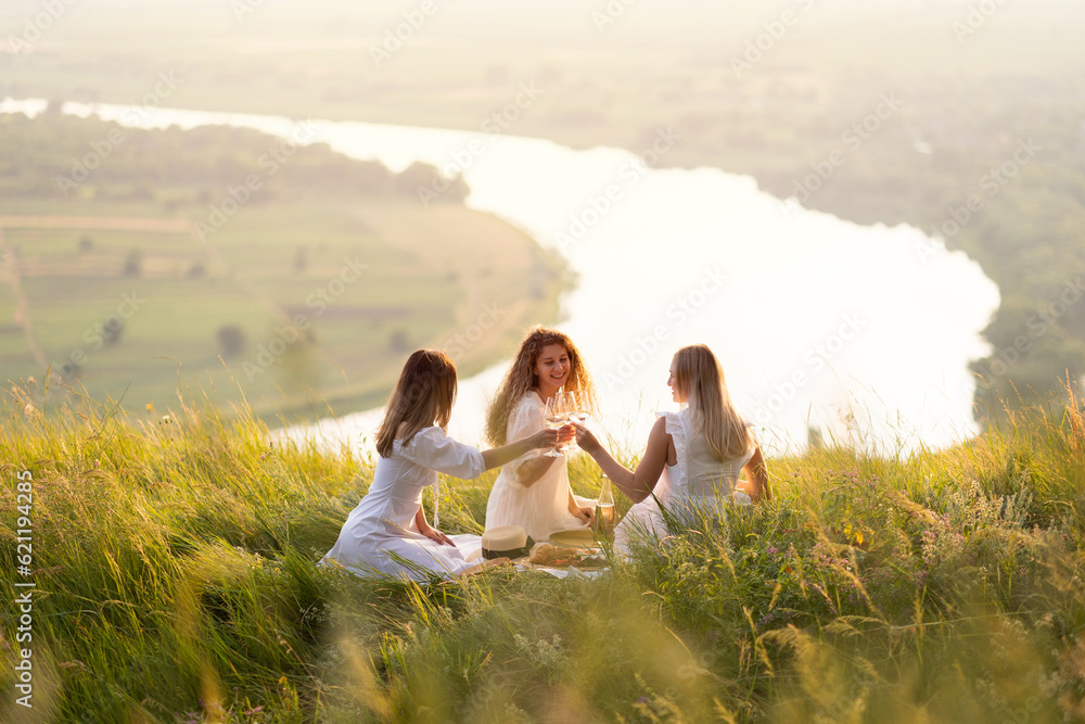 Lovely ladies drinking wine at sunset. Summer happy mood. Girlfriends relaxing on summer sunset with river on the background.