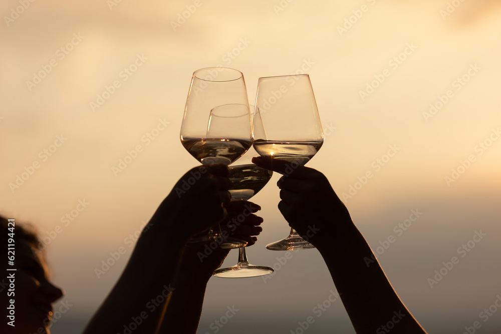 Group of friends with white wine in hands clinking with glasses. Close-up of hands and drinks. Beautiful scenic sunset.
