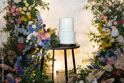 Obraz na płótnie White wedding cake in the evening. Cake on the background of an arch of fresh flowers. w salonie