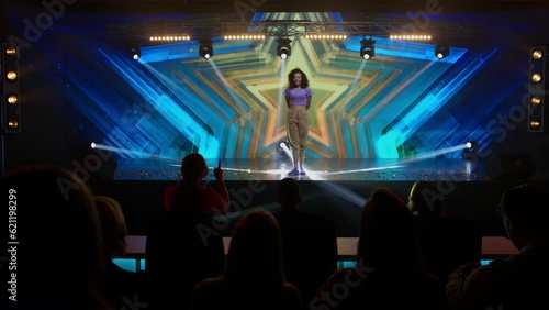 Judges press the golden buzzer to send a contestant to a show finale, the lights changing to gold, young woman dancer talent is happily surprised. Television style broadcast talent show
