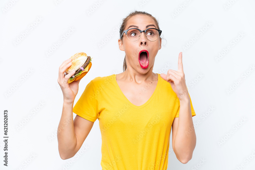 Young caucasian woman holding a burger isolated on white background thinking an idea pointing the finger up