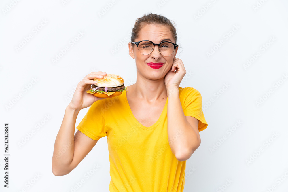 Young caucasian woman holding a burger isolated on white background frustrated and covering ears Young caucasian woman holding a burger isolated on white background frustrated and covering ears