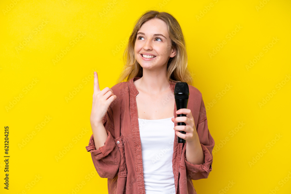 Young singer caucasian woman picking up a microphone isolated on yellow background pointing up a great idea Young singer caucasian woman picking up a microphone isolated on yellow background pointing up a great idea