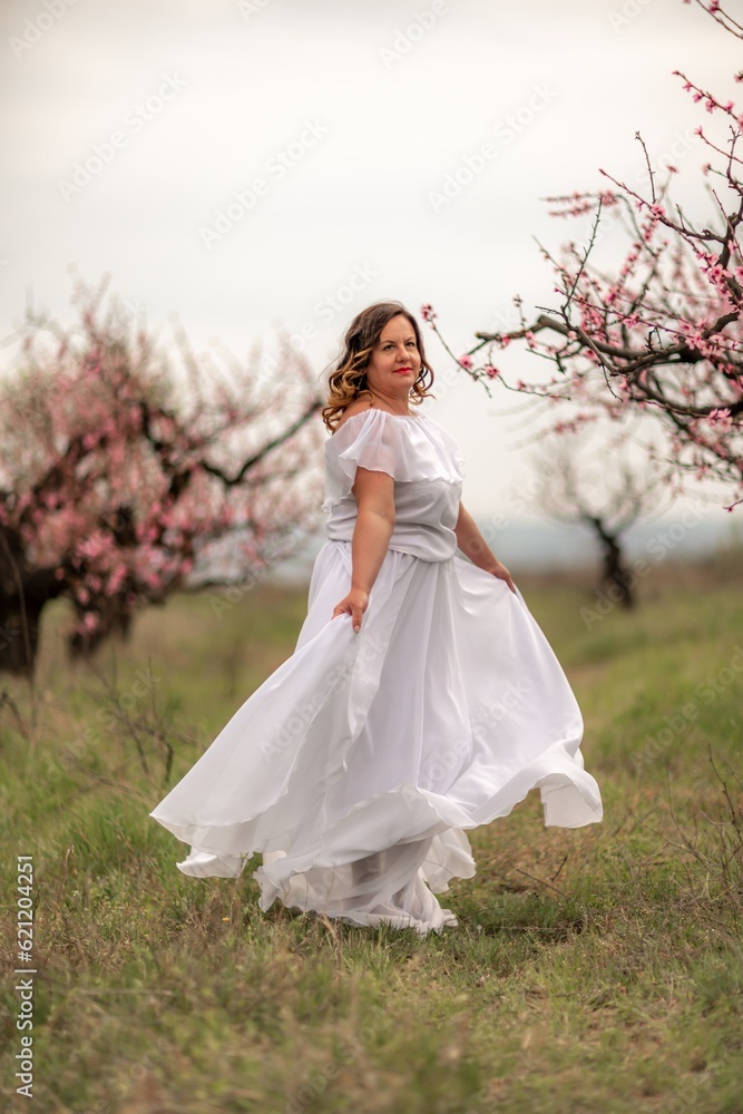 Woman peach blossom. Happy woman in white dress walking in the garden of blossoming peach trees in spring