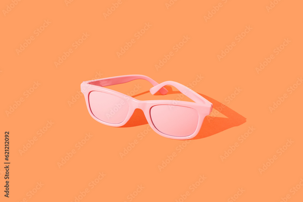 Pink sunglasses in sunlight on orange background. Summer beach party idea. Trendy colorrs.