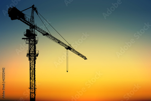A silhouette tower crane for construction with a vibrant sky and early morning light in the background.