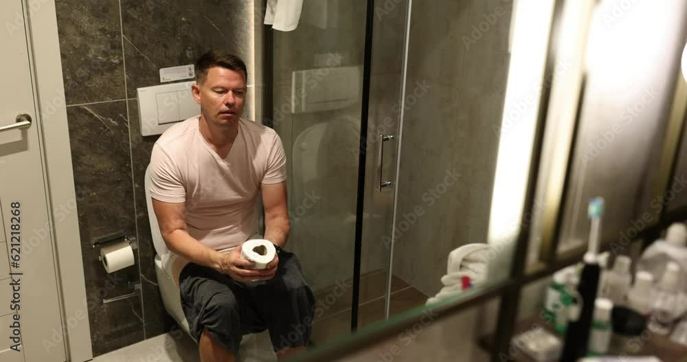 Man suffering from hemorrhoids on toilet in toilet. Guy with diarrhea problem of abdominal pain or cramps Man suffering from hemorrhoids on toilet in toilet. Guy with diarrhea problem of abdominal pain or cramps