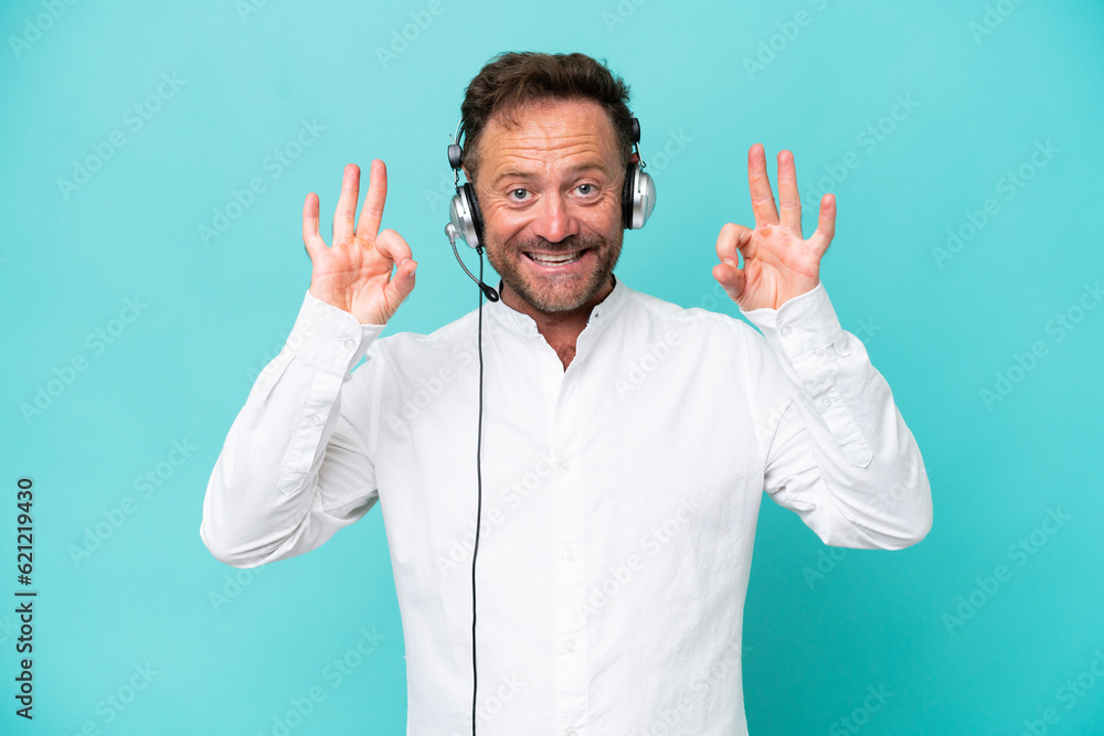 Telemarketer caucasian man working with a headset isolated on blue background showing an ok sign with fingers Telemarketer caucasian man working with a headset isolated on blue background showing an ok sign with fingers
