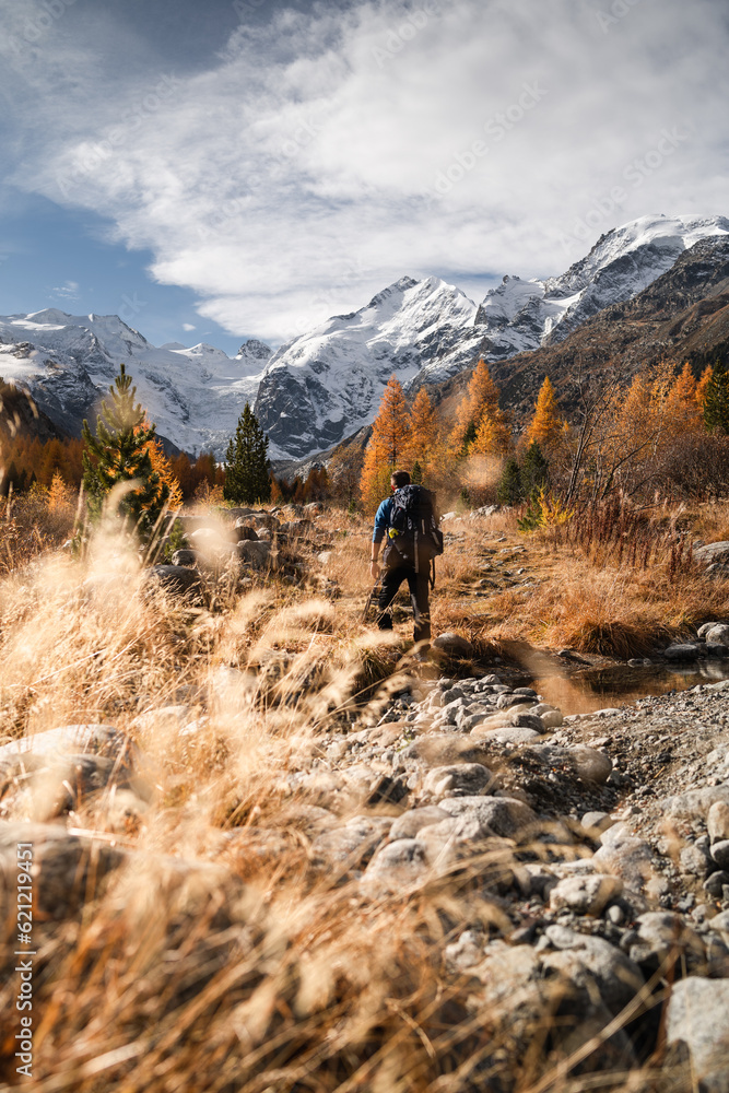 A hiker is walking on the hiking trail of the Morteratsch glacier, during a sunny autumnal day