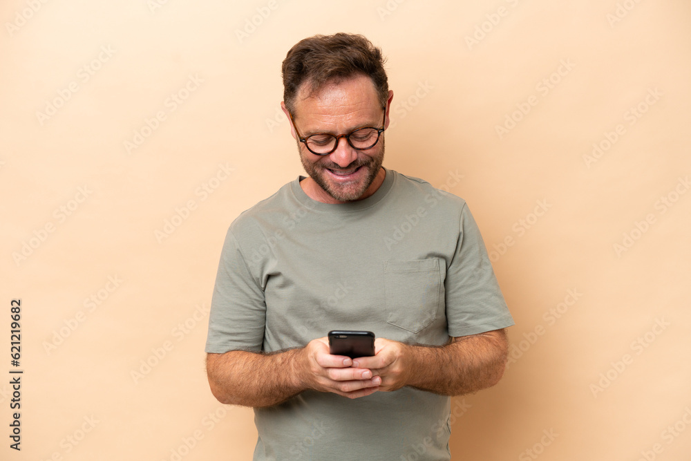Middle age caucasian man isolated on beige background sending a message with the mobile Middle age caucasian man isolated on beige background sending a message with the mobile