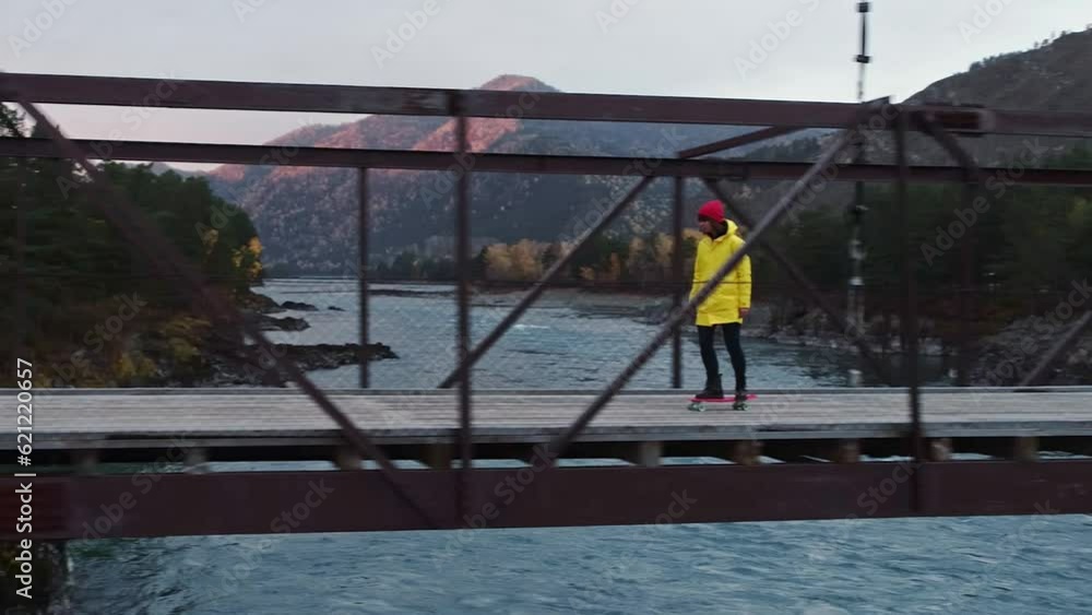Aerial view of young women riding skateboard across the river bridge in mountains nature. Careless girl enjoy travel in green forest landscape background. Freedom holiday inspiration concept Aerial view of young women riding skateboard across the river bridge in mountains nature. Careless girl enjoy travel in green forest landscape background. Freedom holiday inspiration concept