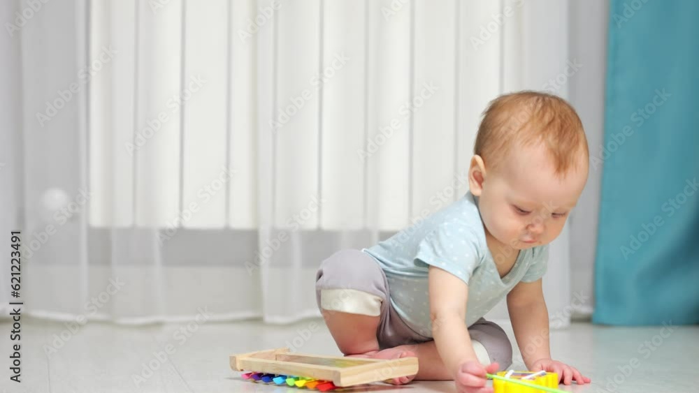 Baby girl plays around with xylophone toy on floor in house. Small child in ordinary clothes learning to play music using colorful toys Baby girl plays around with xylophone toy on floor in house. Small child in ordinary clothes learning to play music using colorful toys