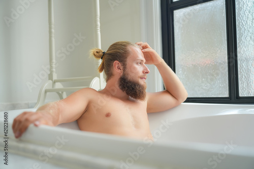 Relaxed young man bathing in modern bathroom luxury interior. Spa, wellness, body care concept