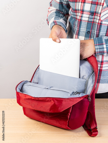 Close-up of a young male student taking out a laptop from a backpack. photo