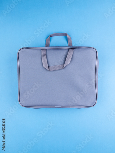 Gray briefcase folder for documents and school items on a bright blue table next to stationery