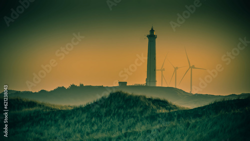 Ein Leuchtturm und eine Gruppe von Windkrafträder bei Sonnenuntergang an der dänischen Nordseeküste