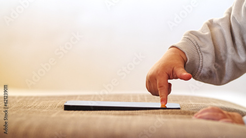 Child's finger pressing, scrolling, tapping on mobile phone screen. Little child learns to use new technologies. Baby pressing with finger on phone touch screen, close-up and soft focus.