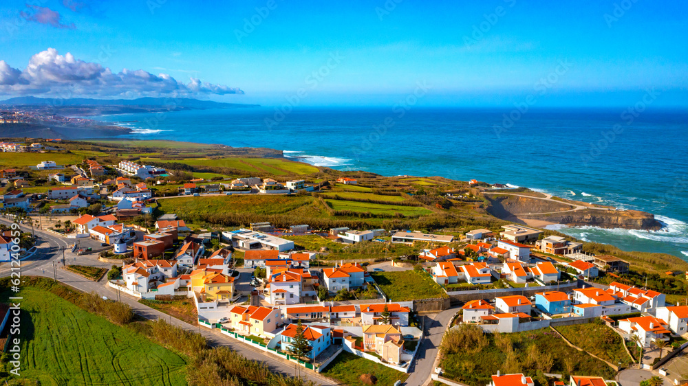 Aerial view of a small European town against blue sky and Atlantic Ocean. Drone view of a beautiful European city with a hilly landscape on ocean background. Beautiful natural landscape. Portugal.