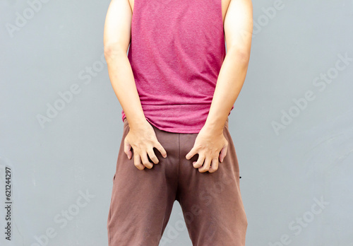 Asian man scratching itch with hand on buttock area, health care concept