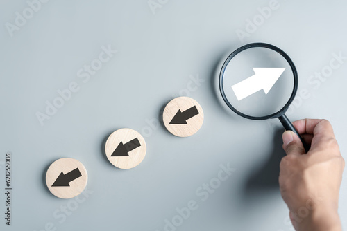 Hand holding magnifier focus to White arrow and different direction facing opposite direction with black arrow for business disruption and technology transformation and different thinking idea photo