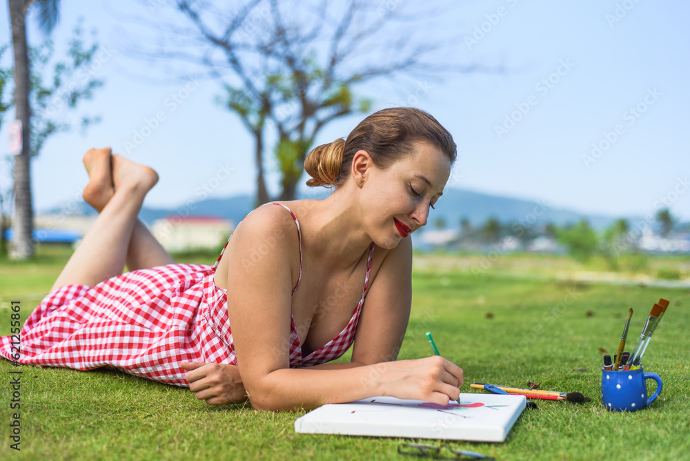 Young woman artist and illustrator drawing witha pencil, laying on a lawn in summer Young woman artist and illustrator drawing witha pencil, laying on a lawn in summer