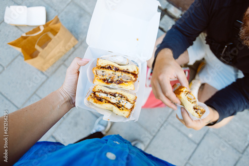 POV top down photo of woman hold delicious sandwich in take away box. Street food festival or food truck concept. Fast food with organic ingridients. Sharing concept photo
