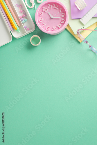 Organized back-to-school setup. Vertical top view of feminine-themed stationery, copybooks, pencil case, tape, ruler, clock, glasses on refreshing teal backdrop. Versatile space for text or advert