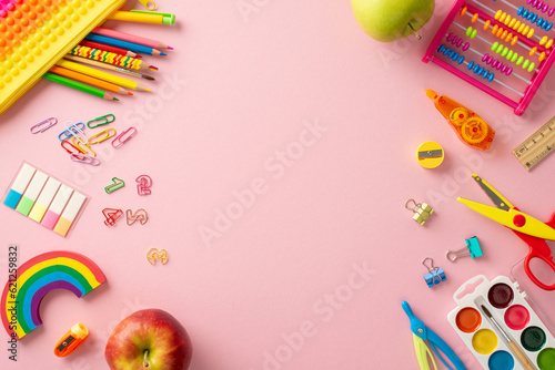 Classroom essentials collection. Top view of vivid assemblage of supplies, pop-it pencil case, paint set for drawing, abacus, apples and more on pink surface. Empty space suitable for text or adverts