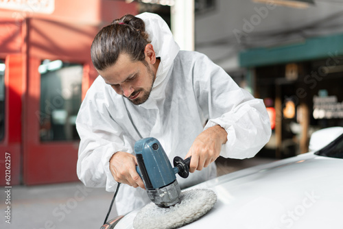 Caucasian man holds a polisher in the hand and polishes the car at car service 