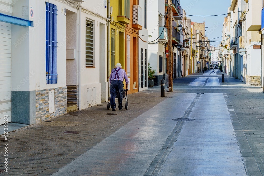 Barcelona, Spain- June 6, 2023. Elderly disabled patient walking slowly with a walker in the street. Elderly disabled adults feel painful and suffer from back pain. Medical therapy insurance concept