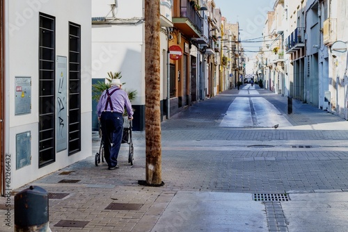 Barcelona, Spain- June 6, 2023. Elderly disabled patient walking slowly with a walker in the street. Elderly disabled adults feel painful and suffer from back pain. Medical therapy insurance concept © Manuel Milan