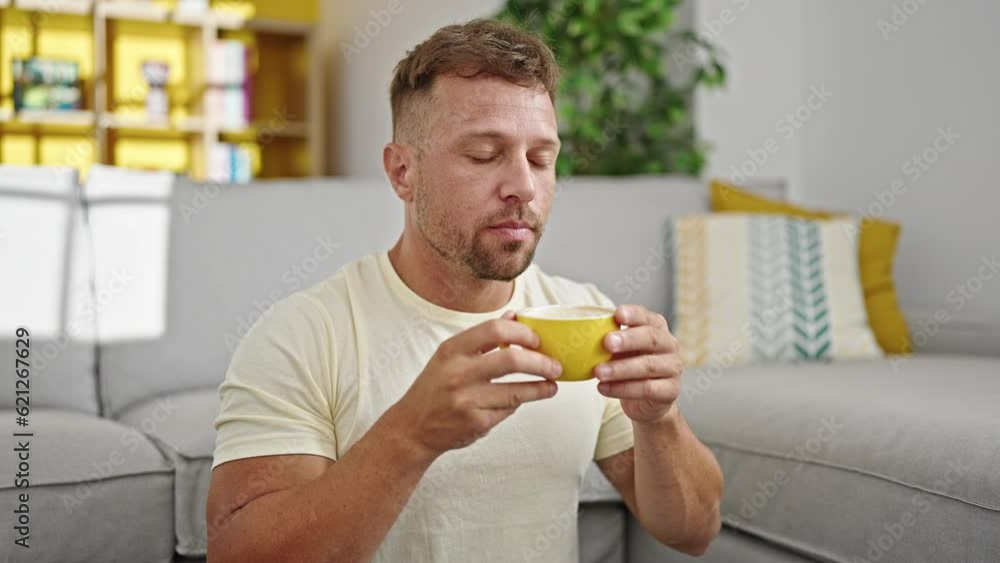 Young man drinking coffee sitting on floor at home Young man drinking coffee sitting on floor at home