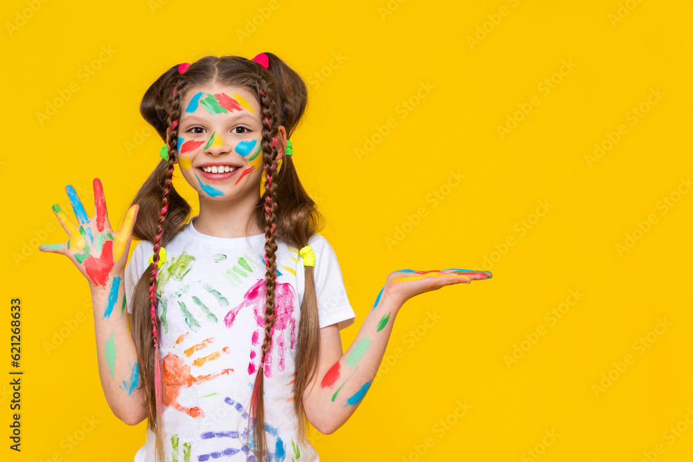 A child smeared with paint. A little girl, painted with multicolored paints, holds your advertisement in the palm of her hand. Children's creativity. Yellow isolated background. Copy space. Banner. A child smeared with paint. A little girl, painted with multicolored paints, holds your advertisement in the palm of her hand. Children's creativity. Yellow isolated background. Copy space. Banner.