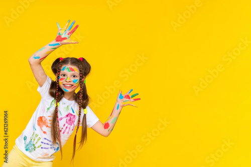 A child painted with multicolored paints. A young girl with painted palms. Creativity for schoolchildren. Drawing for children. Yellow isolated background. Copy Space.