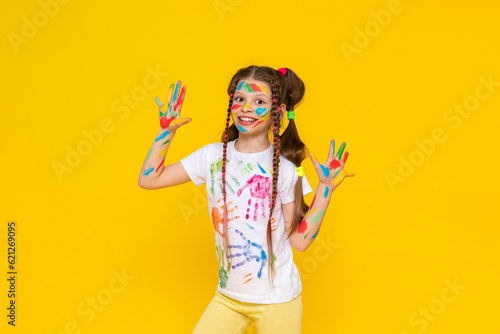 A child painted with multicolored paints. A young girl with painted palms. Creativity for schoolchildren. Drawing for children. Yellow isolated background.