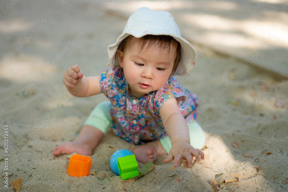 Adorable 9 months old baby playing outdoors - lifestyle portrait of mixed ethnicity Asian Caucasian baby girl playing with block toys happy and carefree at playground sitting on sand Adorable 9 months old baby playing outdoors - lifestyle portrait of mixed ethnicity Asian Caucasian baby girl playing with block toys happy and carefree at playground sitting on sand