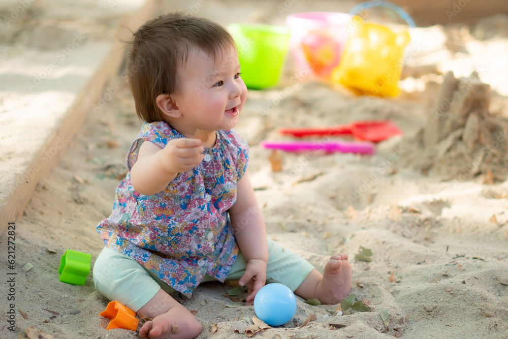 Adorable 9 months old baby playing outdoors - lifestyle portrait of mixed ethnicity Asian Caucasian baby girl playing with block toys happy and carefree at playground sitting on sand Adorable 9 months old baby playing outdoors - lifestyle portrait of mixed ethnicity Asian Caucasian baby girl playing with block toys happy and carefree at playground sitting on sand