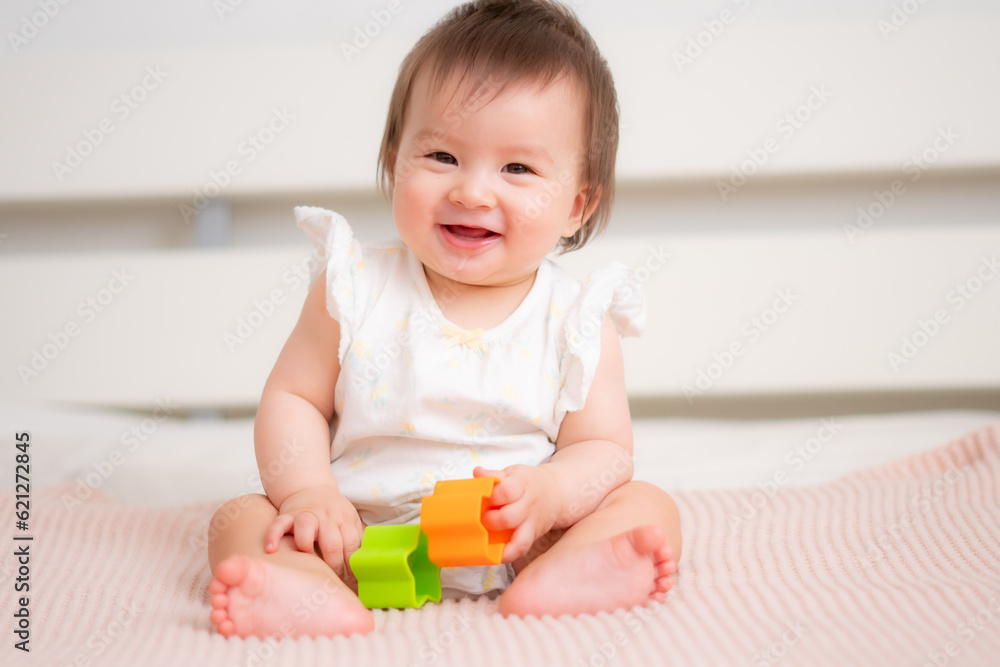 lifestyle home portrait of 9 months old mixed ethnicity Asian Caucasian baby girl playing happy and carefree on bed crawling and handling color blocks in childhood and nursery concept lifestyle home portrait of 9 months old mixed ethnicity Asian Caucasian baby girl playing happy and carefree on bed crawling and handling color blocks in childhood and nursery concept
