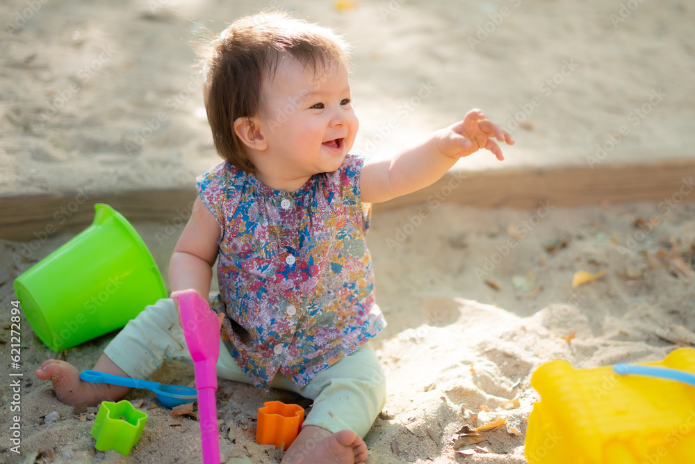 Adorable 9 months old baby playing outdoors - lifestyle portrait of mixed ethnicity Asian Caucasian baby girl playing with block toys happy and carefree at playground sitting on sand Adorable 9 months old baby playing outdoors - lifestyle portrait of mixed ethnicity Asian Caucasian baby girl playing with block toys happy and carefree at playground sitting on sand