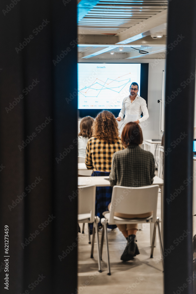 Business trainer sharing business knowledge and guidance for better profit growth to a group of young intelligent businesspeople Business trainer sharing business knowledge and guidance for better profit growth to a group of young intelligent businesspeople