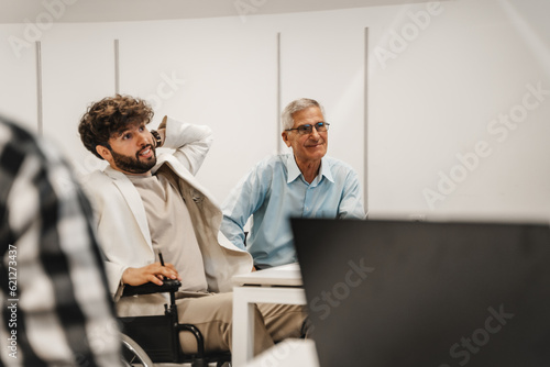 Smiley  good looking  mature businessman listening to a presentation at the classroom with his handicapped junior male colleague