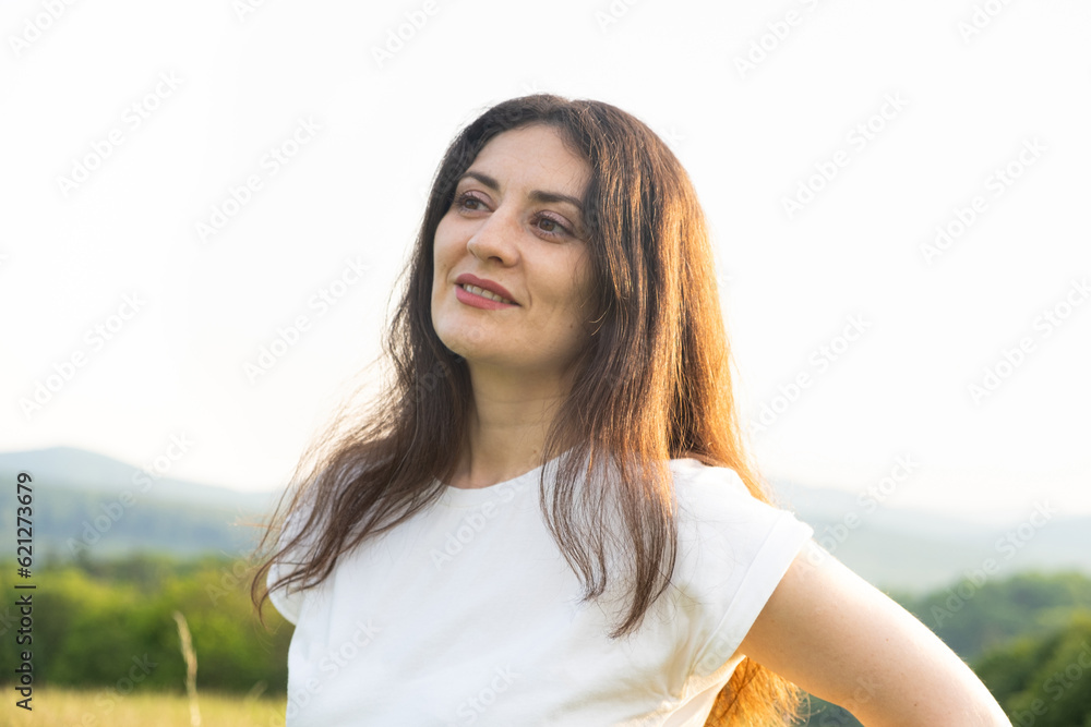 Fototapeta premium Portrait of a pensive 35-year-old woman in a white T-shirt against the sky in nature in summer.