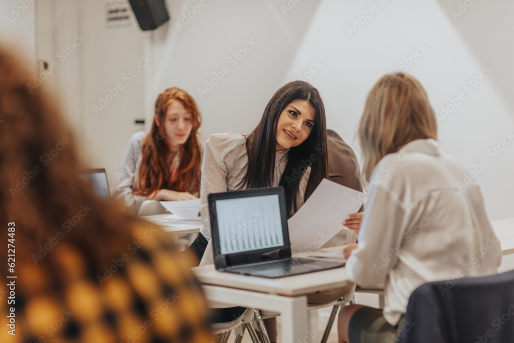 Brunette female worker discussing financial reports with her blonde colleague during brainstorming at the classroom Brunette female worker discussing financial reports with her blonde colleague during brainstorming at the classroom