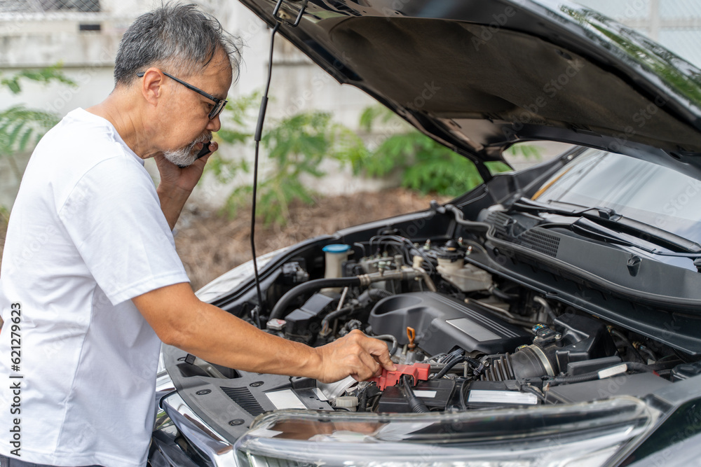 Middle age man checking his broken down car's engine while on the phone with a mechanic Middle age man checking his broken down car's engine while on the phone with a mechanic