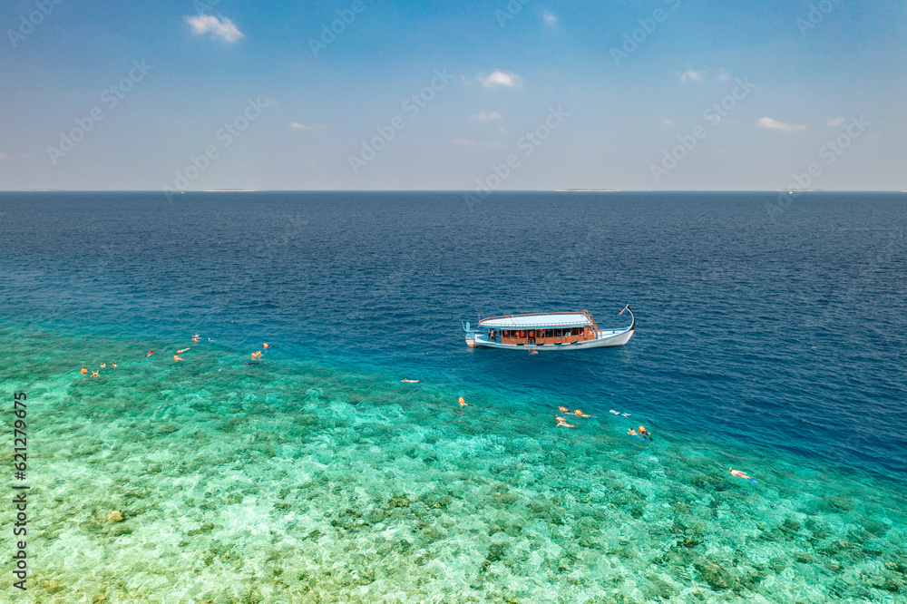 Maldives aerial travel. Dhoni sailing boat next to sea bay coral reef. Bird eye view water sport theme. Snorkel excursion, recreational diving with tourist people. Luxury water sport outdoors activity
