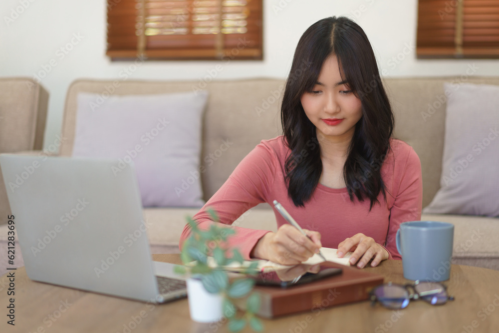 Young businesswoman writing down idea about new startup project in notebook while working at home Young businesswoman writing down idea about new startup project in notebook while working at home