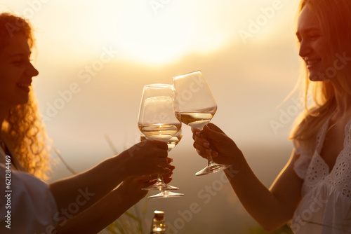 Obraz na płótnie A group of happy smiling girlfriends raise a toast with glasses of white wine on a sunset. Close shot. w salonie